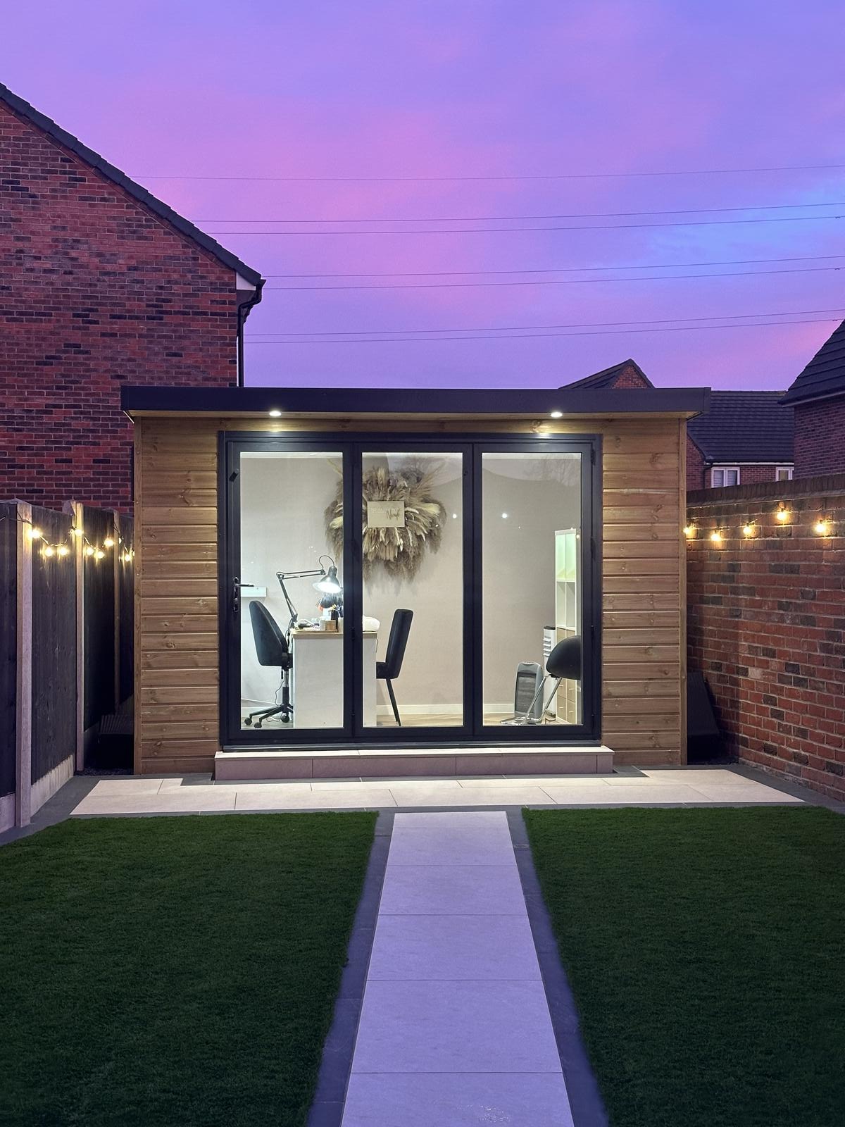 Nicole's salon at dusk, a timber cabin with glass doors and the nail desk lit inside